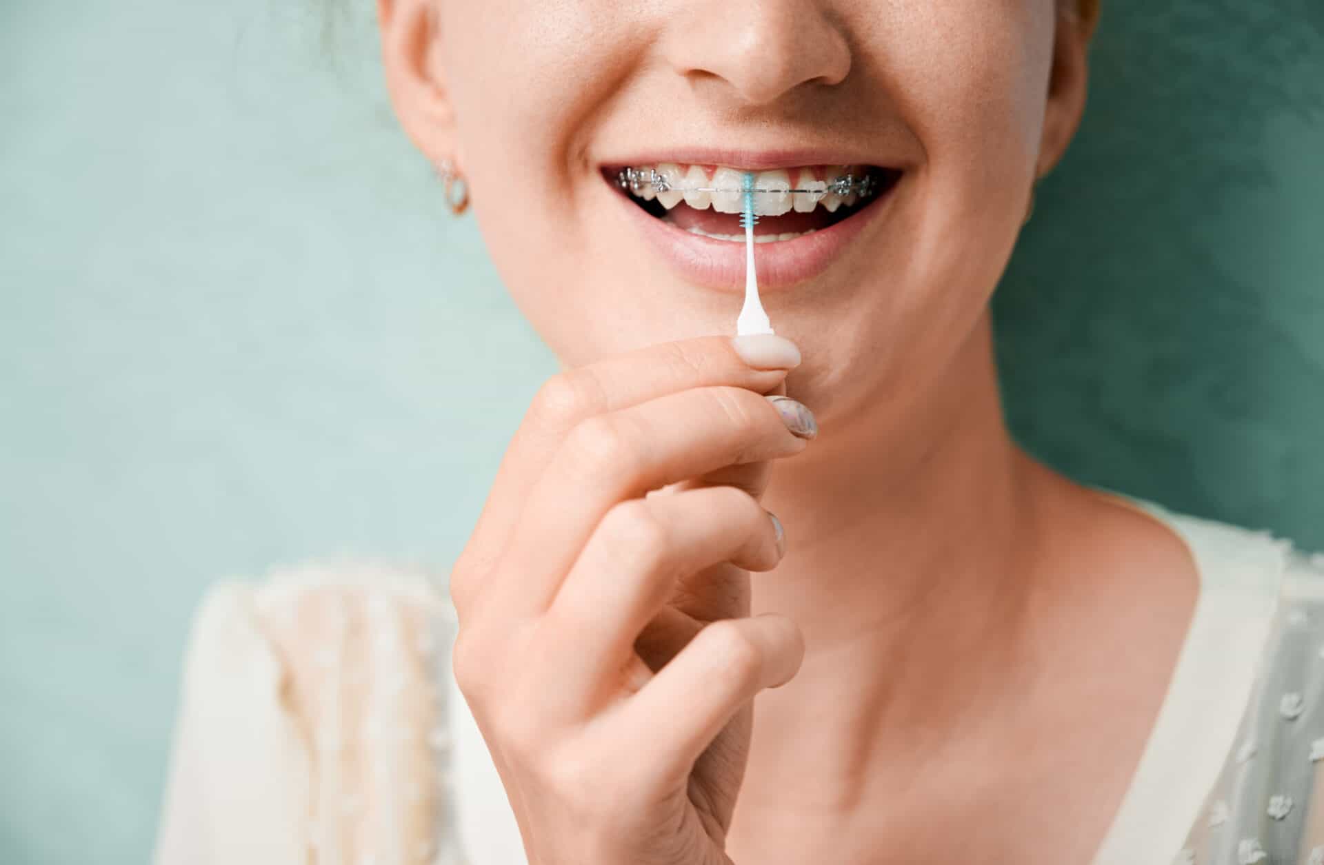 Close up of woman using elastic cleaning toothpick while brushing teeth with orthodontic brackets. Woman cleaning teeth with dental floss brush. Concept of dentistry, hygiene and dental care.