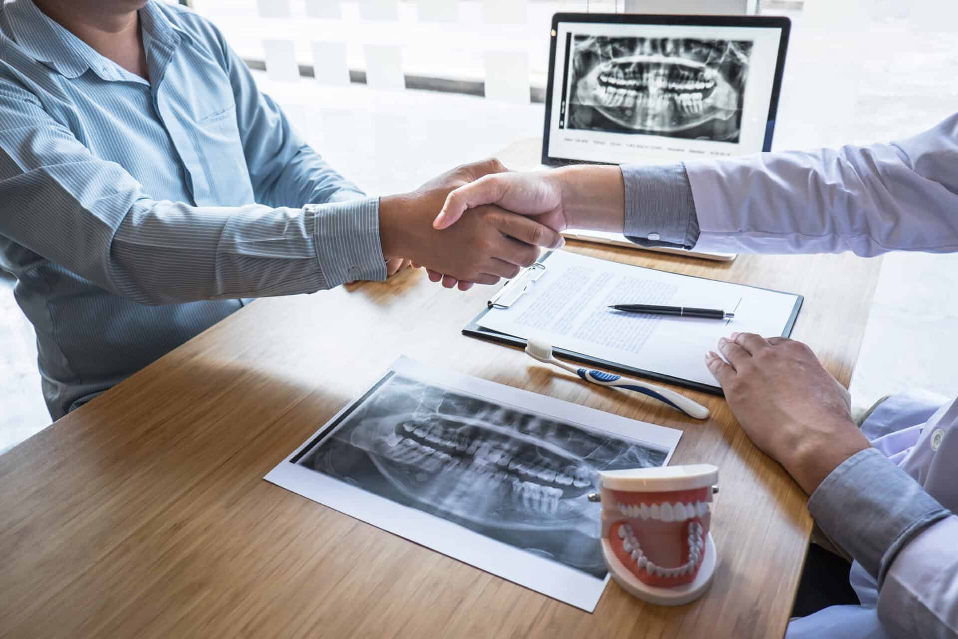 Professional Dentist showing jaw and teeth the x-ray photograph and shaking hands after finish discussing during explaining the consultation treatment issues with patient